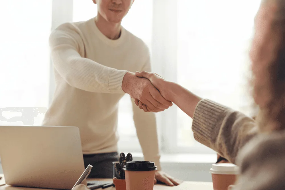 Two professionals shaking hands across a desk, symbolizing a successful job offer for an instructional designer.
